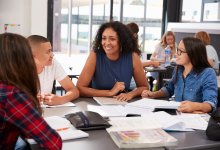 A teacher talking to her high school students at a table in a classroom